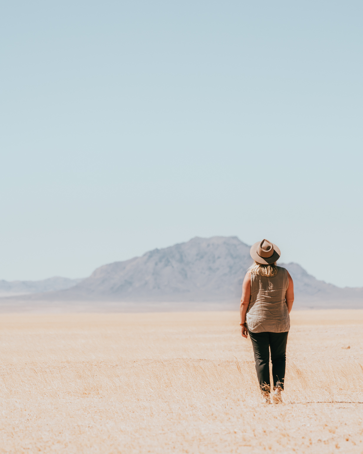 A girl in a hat stands in the desert in Namibia, looking at the distant mountains