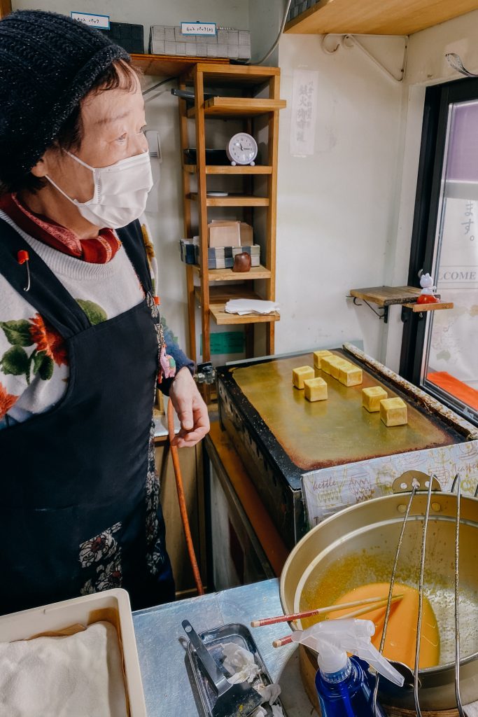 a woman making a sweet treat at miyagawa morning market in takayama