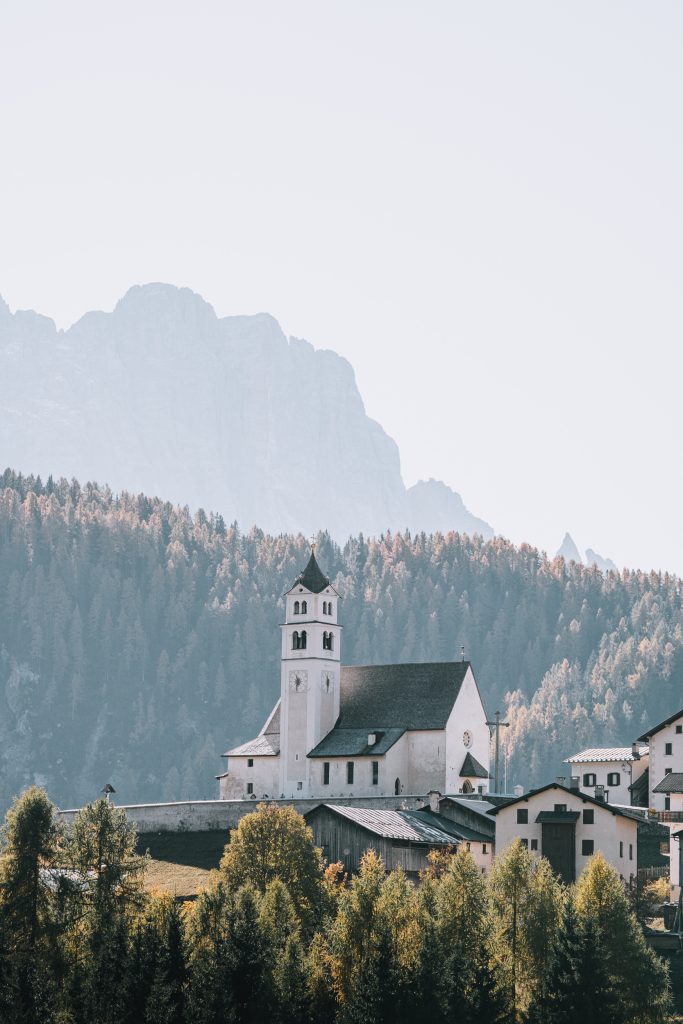 A white church with mountain peaks in the foreground and background - stopping at random villages is on of my favourite things to do in the Dolomites for views like these