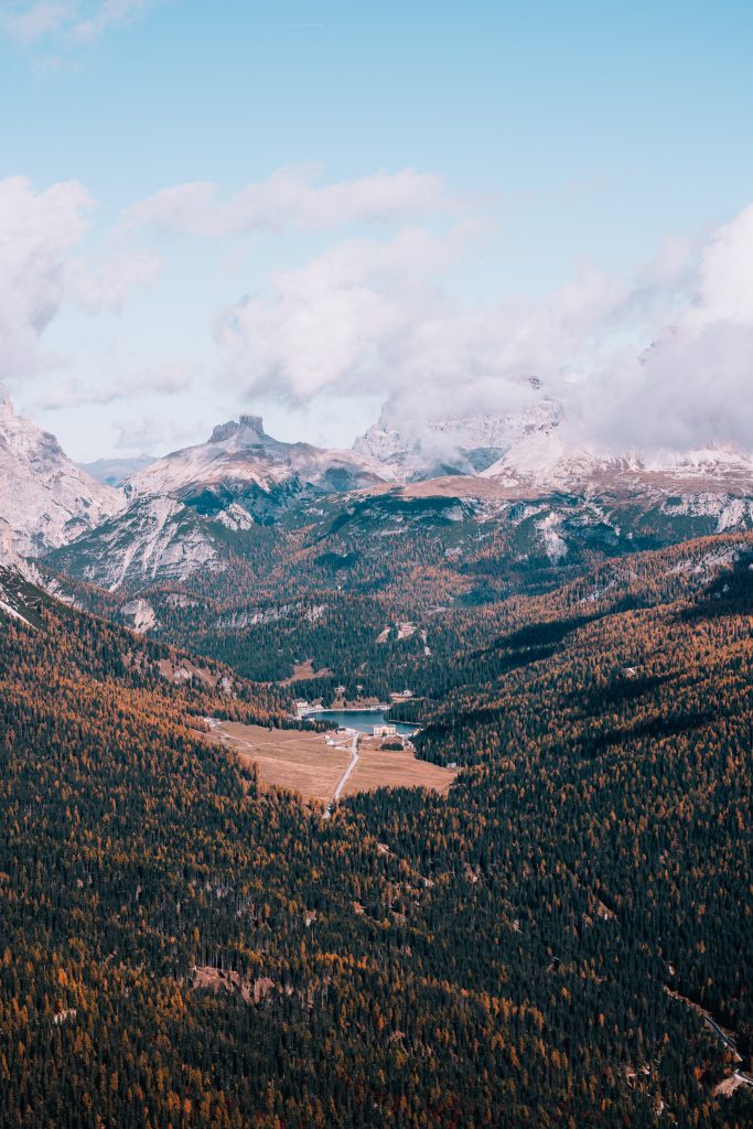 mountainsides covered in trees with a small lake in the distance and towering mountains in the background which are classic views when visiting the dolomites