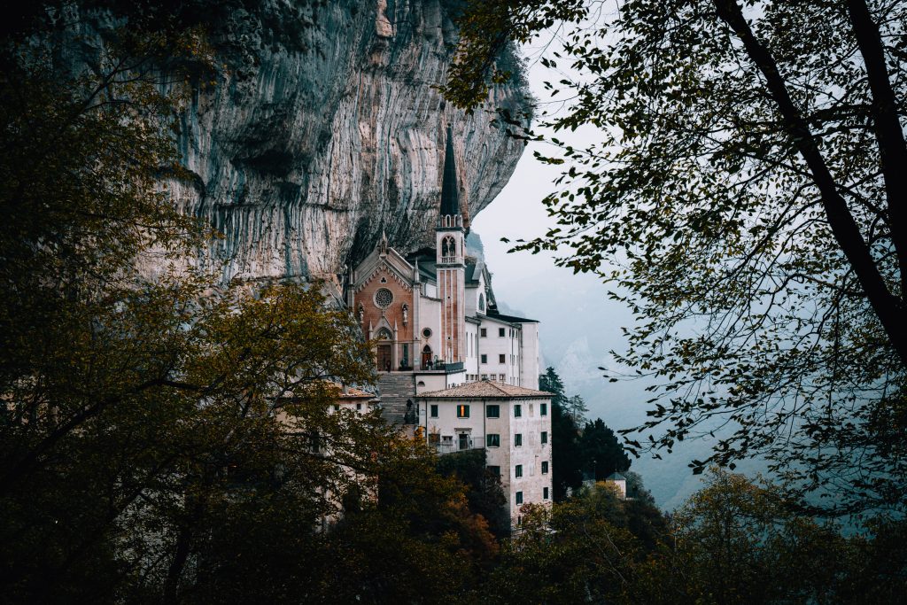 A church and convent nestled under a mountain, built into the side of the cliff with mist in the background
