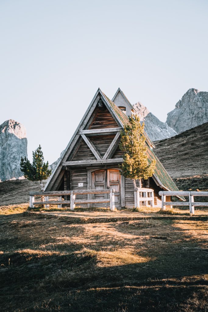 A cute A-frame wooden mountain hut with the grey peaks of the Dolomites half-hidden behind