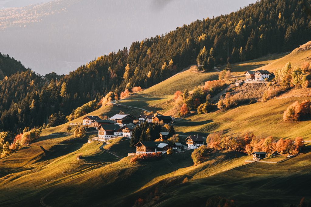 Whitewash and wood chalets sitting on rolling hills in a green and orange autumnal landscape in Val do Funes