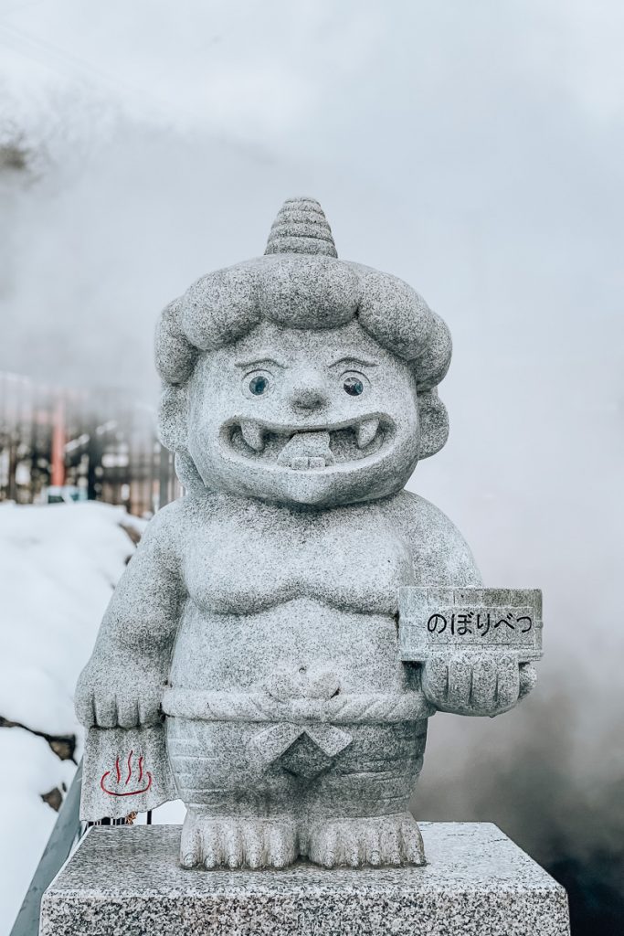 A smiling stone devil statue warning of hot steam in Noboribetsu Onsen Japan